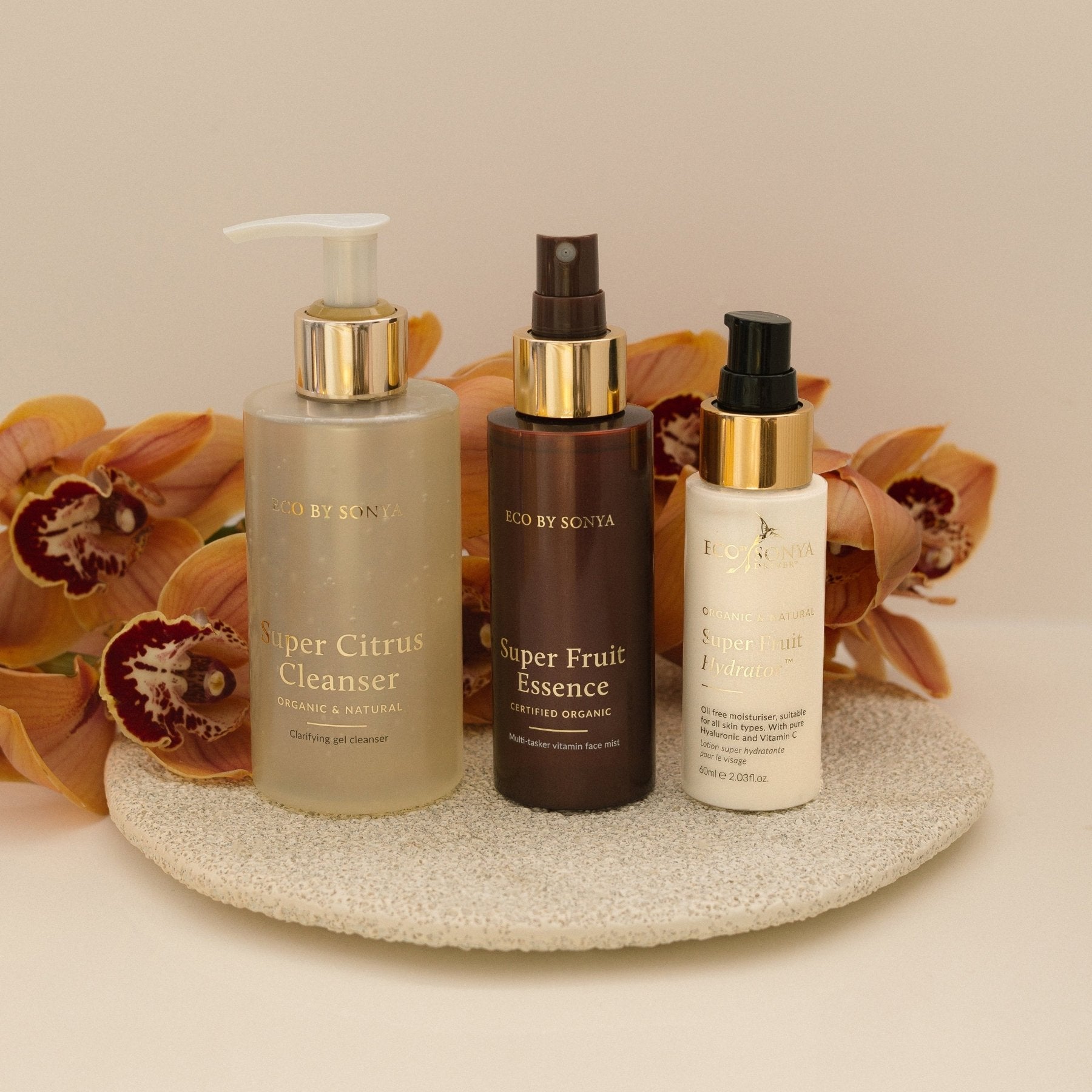 Eco By Sonya 3 step skincare system with Super Citrus Cleanser, Super Fruit Essence and Super Fruit Hydrator on a decorative plate with flowers in the background