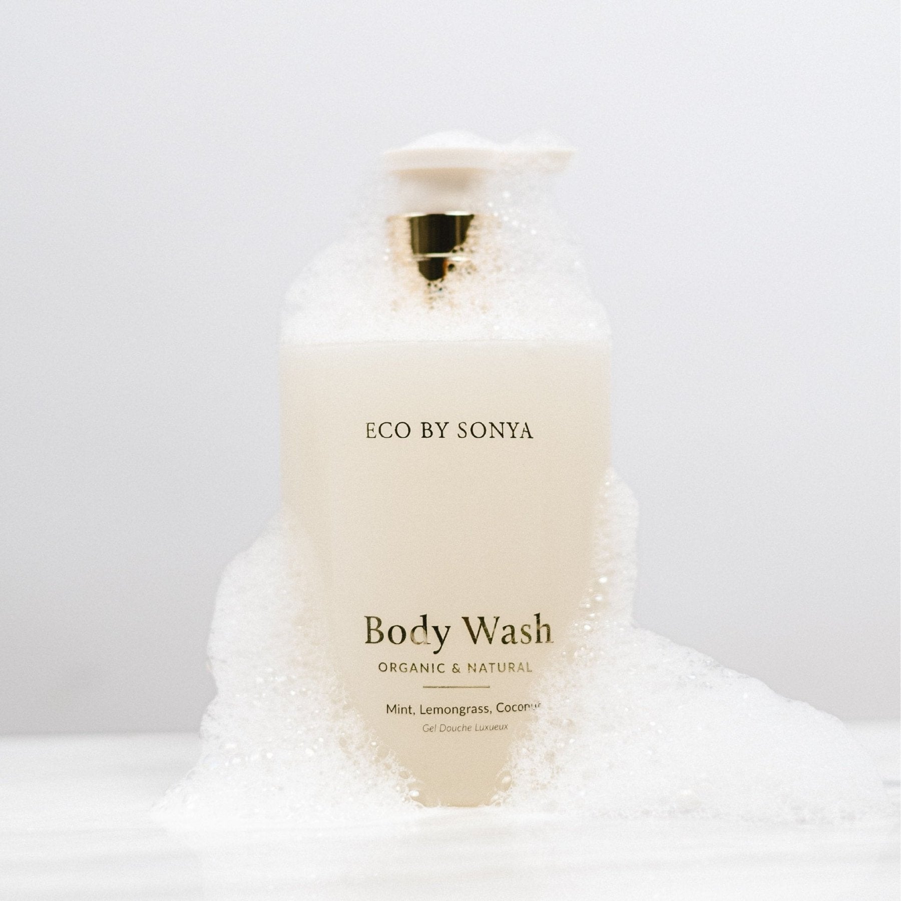 ECO BY SONYA Body Wash bottle surrounded by white foam against a clean white background.