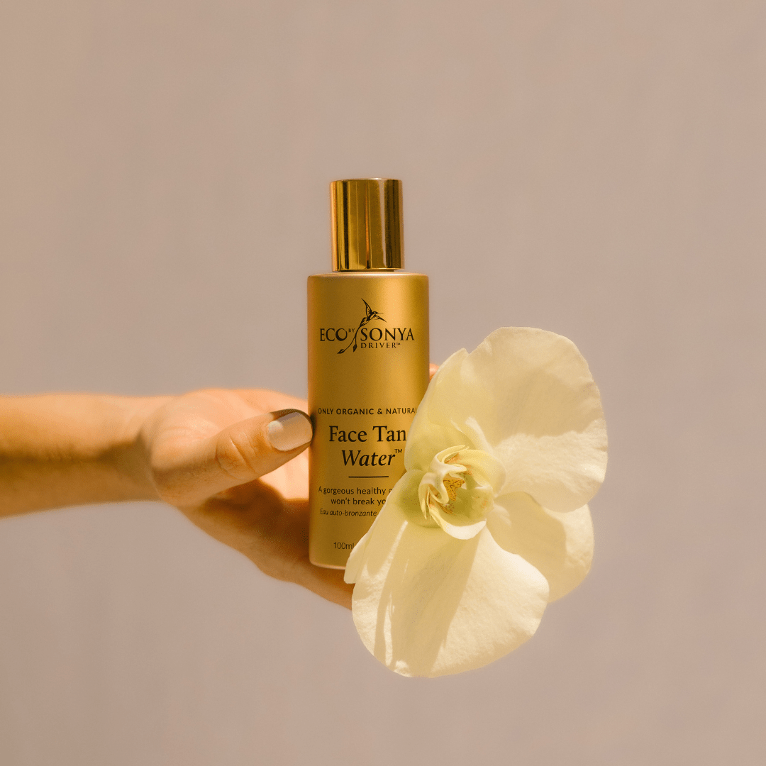 Hand holding Eco By Sonya Face Tan Water bottle beside white flower, organic natural Australian made sunless face tanner.