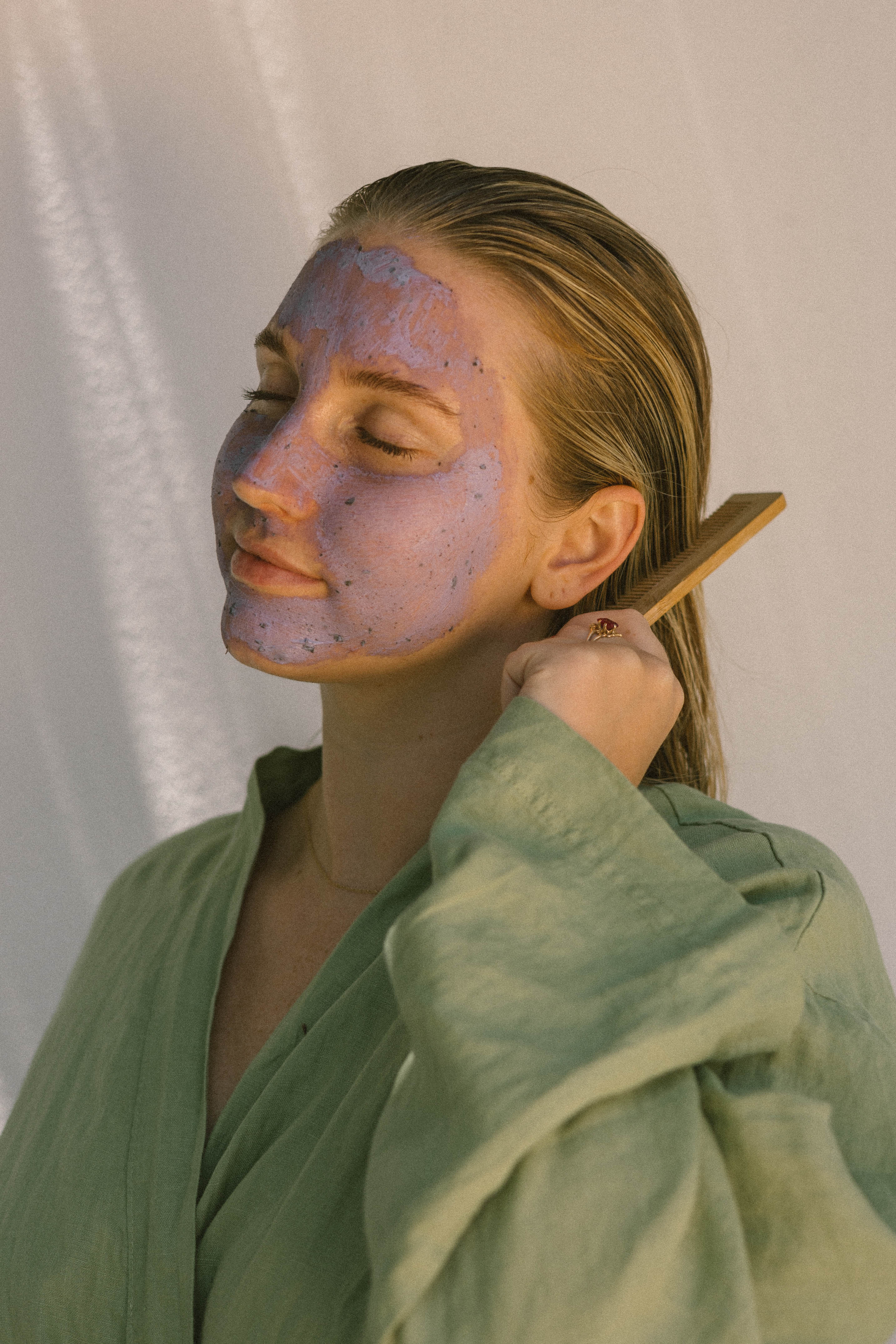 Woman with a Face Compost Purple Mask brushing her hair with a wooden comb 
