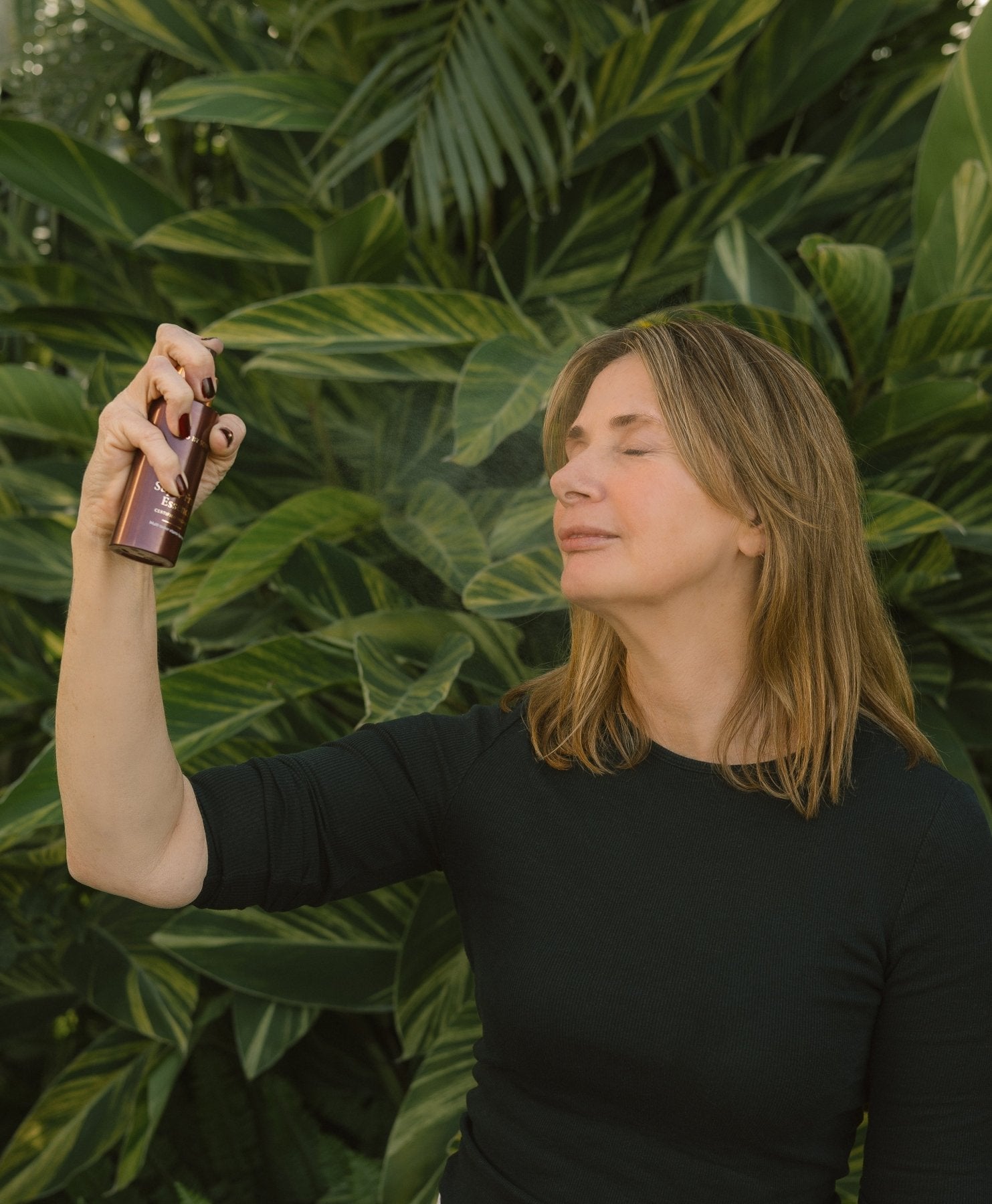 Woman spraying Super Fruit Essence onto her face, against a green leafy background