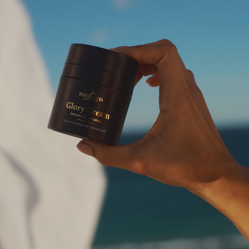 Woman applying Eco By Sonya Glory Cream rich moisturiser to her face in warm sunlight, showing smooth creamy texture and relaxed expression.